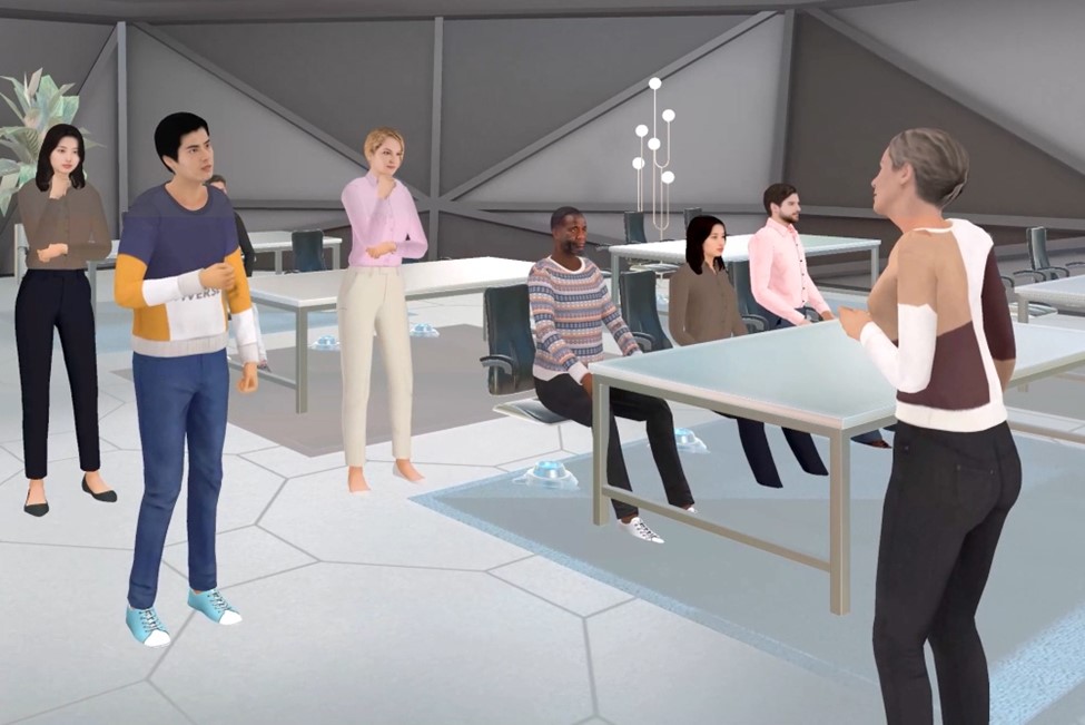A virtual reality scene depicting a classroom with multiple user avatars standing and sitting around desks while watching another user avatar give a presentation.