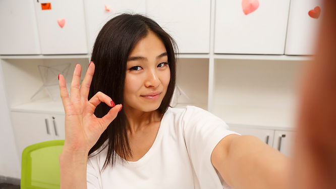 Selfie of a long-haired woman making an OK gesture with her fingers.